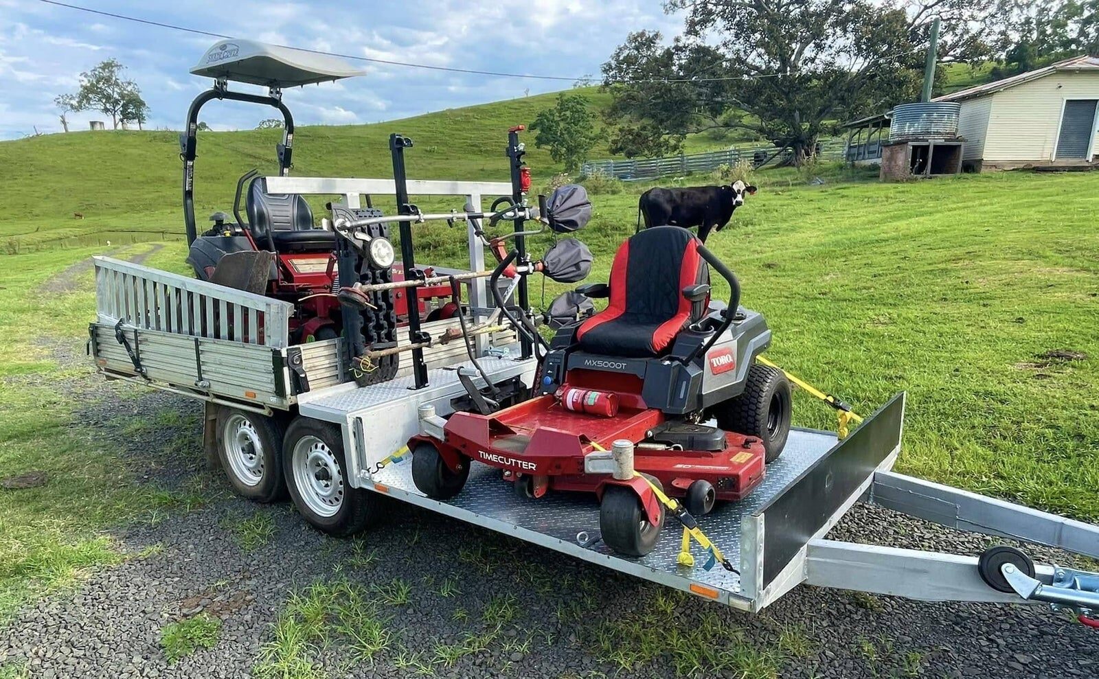 Trailer loaded with a zero-turn mower and equipment in front of green rolling hills